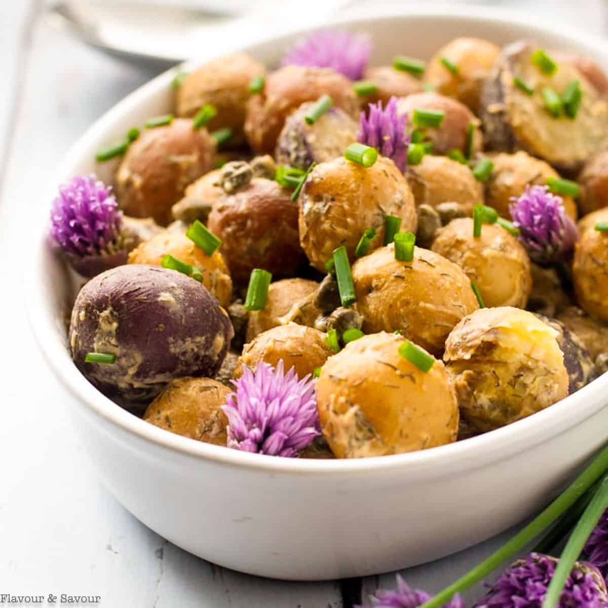 A bowl of potato salad garnished with chives and chive flowers.