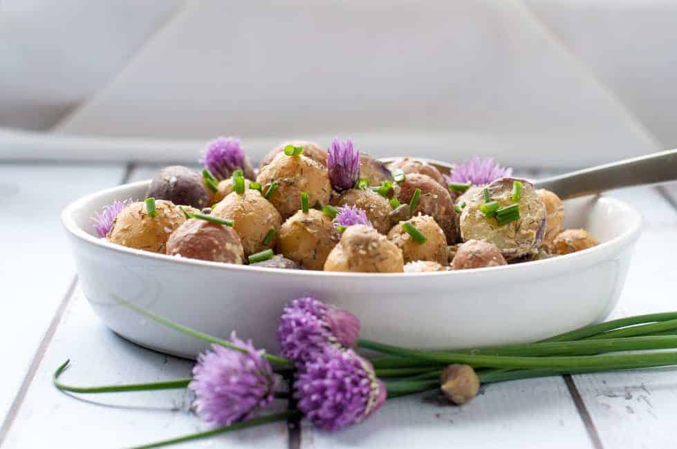 Springtime Potato Salad with Lemon Tahini Dressing in a white oval bowl with purple chive flowers.