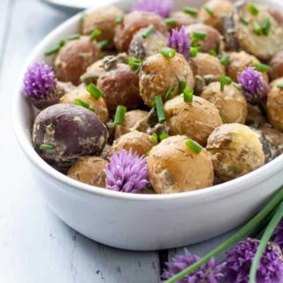 Springtime Potato Salad with Lemon Tahini Dressing in an oval bowl with chive flowers.