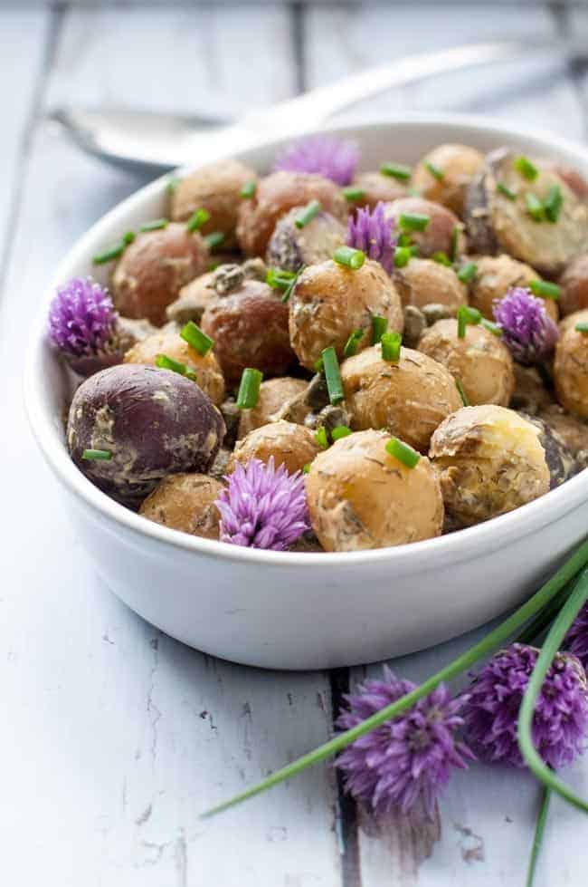 Springtime Potato Salad with Lemon Tahini Dressing in an oval bowl with chive flowers.
