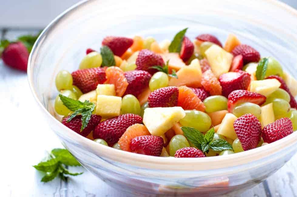  Tropical Fruit with honey mint lime syrup in a bowl with mint sprigs.