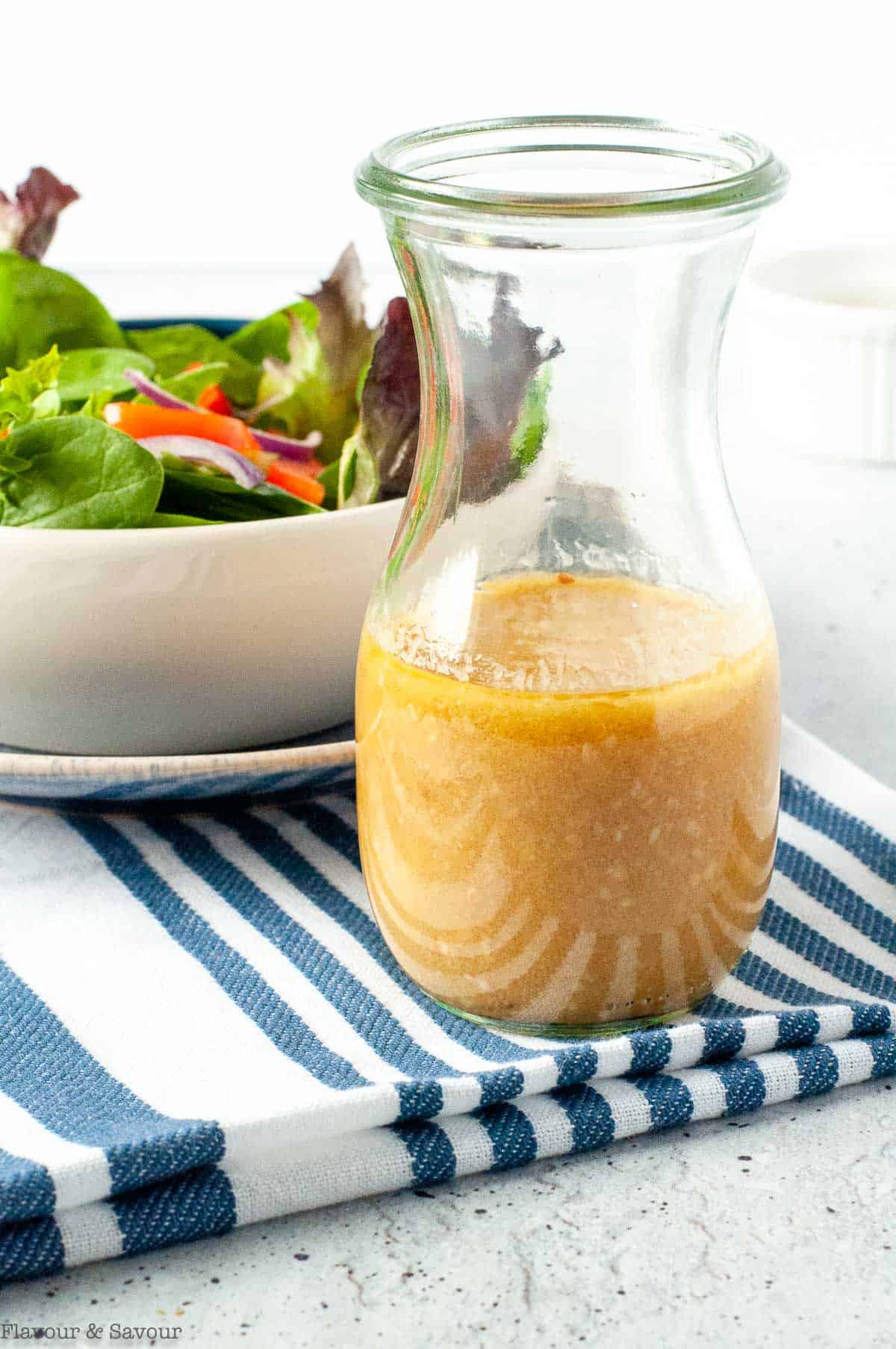 A flask with miso vinaigrette with a salad in the background.