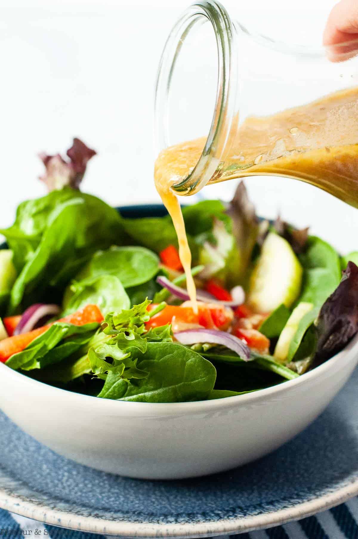 Pouring Asian dressing on a salad.