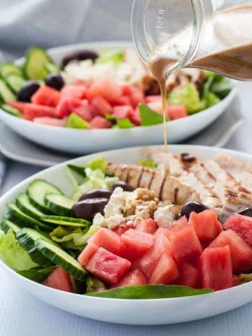 Pouring dressing on Skinny Greek Chicken Bowl with Watermelon and Feta