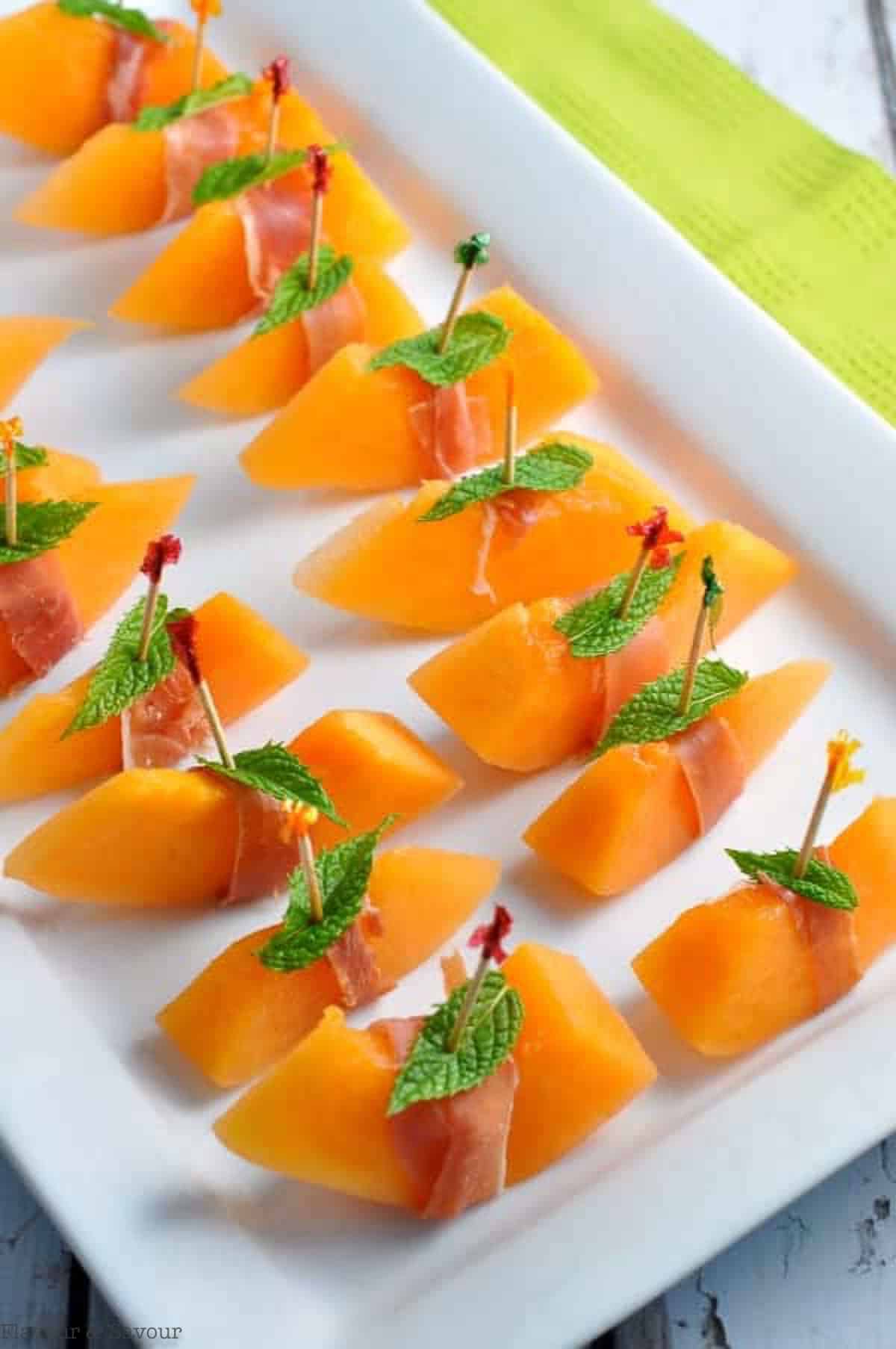 a tray of skewered melon wrapped with prosciutto