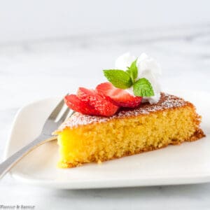 a slice of flourless almond cake topped with strawberry slices and coconut whip