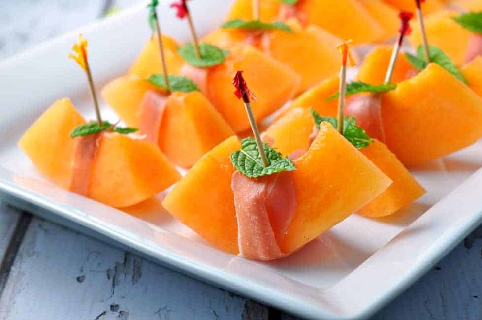 small slices of cantaloupe melon wrapped with a thin slice of prosciutto,  and skewered with a mint leaf 
