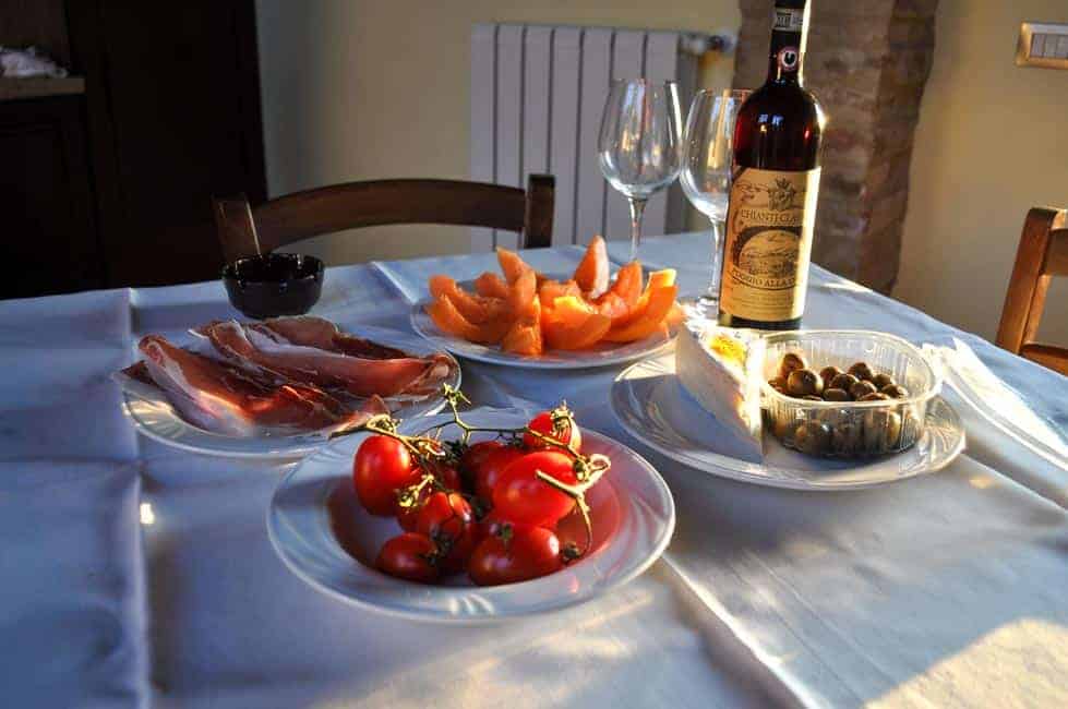 A table with fresh prosciutto, melon slices, olives, cheese, tomatoes and wine in Tuscany