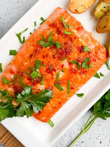 Honey Citrus Glazed Salmon filet on a white platter with air-fried potatoes.