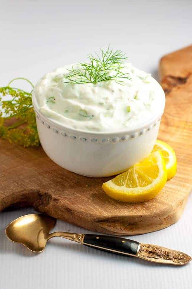 Homemade creamy Tzatziki Sauce, made with yogurt, cucumber, lemon, garlic and dill in a small bowl with lemon slices.