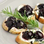 Roasted Cherry Whipped Goat Cheese Crostini appetizers on a plate with a sprig of rosemary