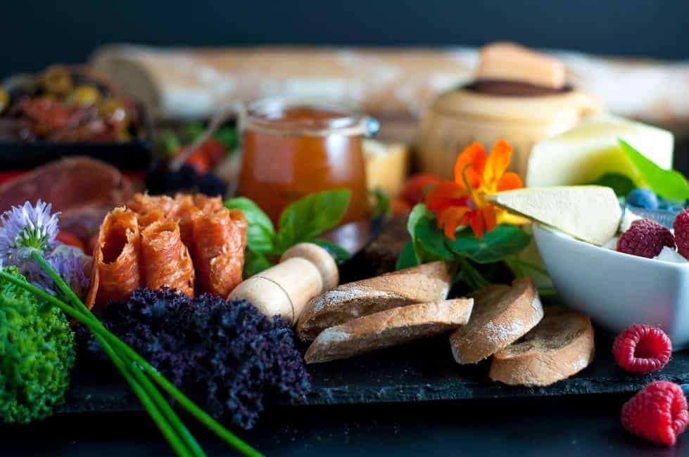 How to Make an Antipasto Platter. An assortment of cheese, charcuterie, olives, fresh vegetables, berries, preserves, herbs and edible flowers on a slate tray.