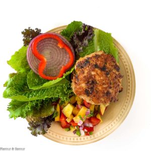 Chipotle Chicken Burger with a slice of red onion and red pepper with greens and peach salsa