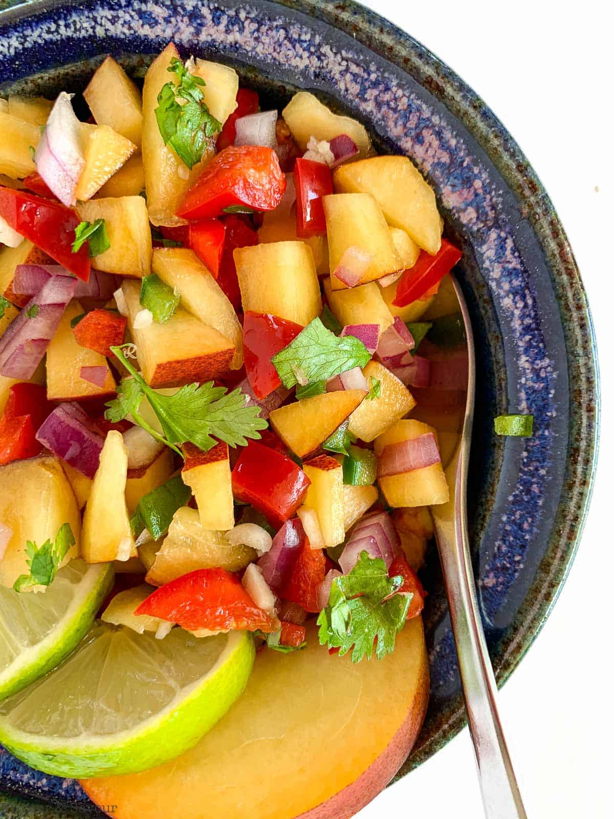 Peach Salsa in a blue bowl with slices of lime.