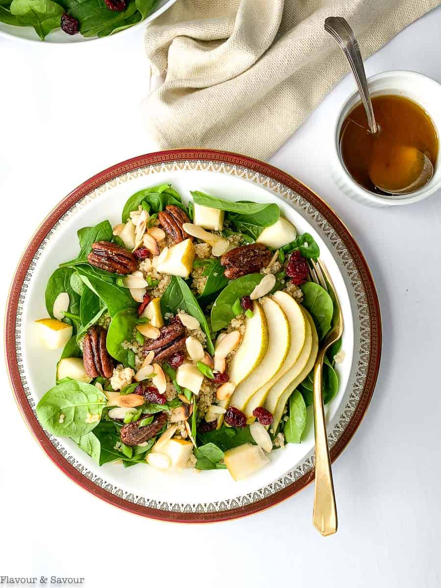 Overhead view of Harvest Quinoa Salad on a red-rimmed plate with a bowl of dressing beside.