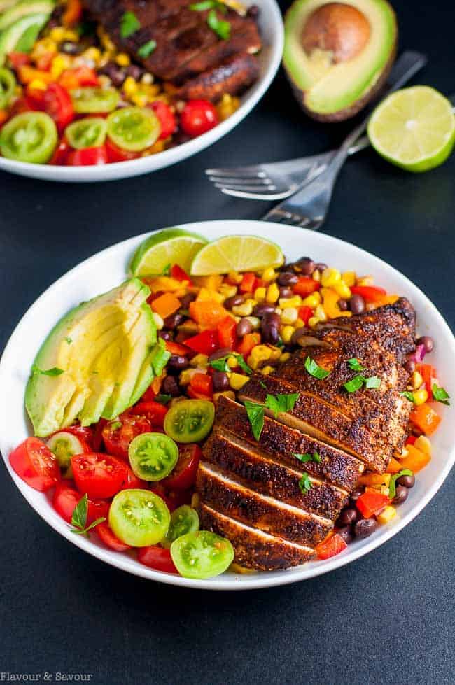 Southwestern Fajita Baked Chicken Bowl with sliced chicken breast, corn, black bean, pepper and tomato chopped salad with sliced avocado in a bowl.