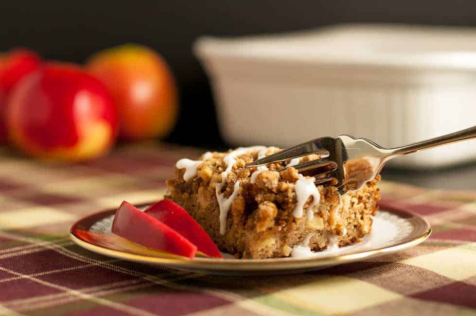 A forkful of Gluten-Free Apple Cinnamon Coffee Cake with apples in the background