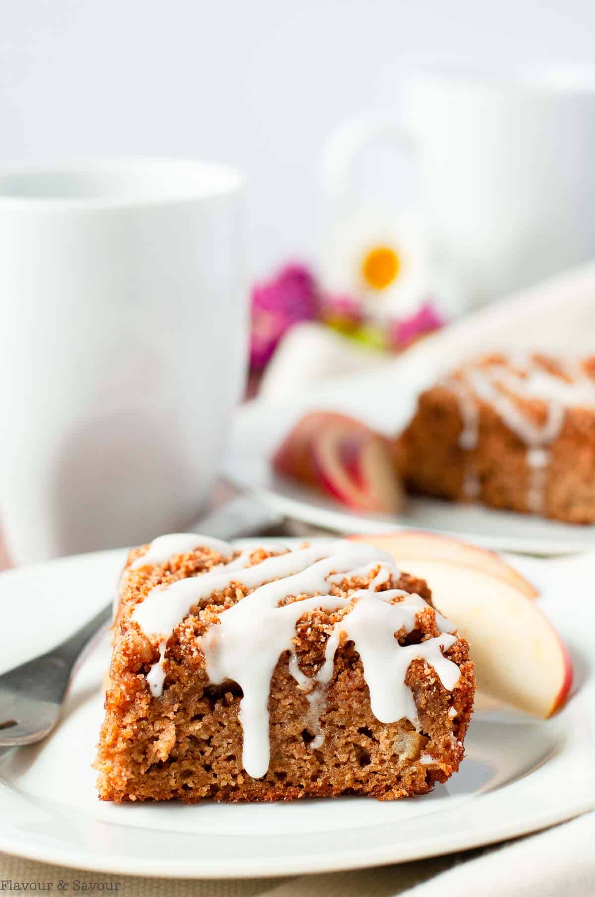 Gluten-free apple cinnamon coffee cake with a lemon drizzle on a plate with apple slices.