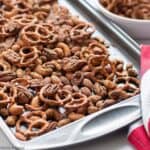 A spicy snack mix made with pretzels and mixed nuts on a baking sheet.