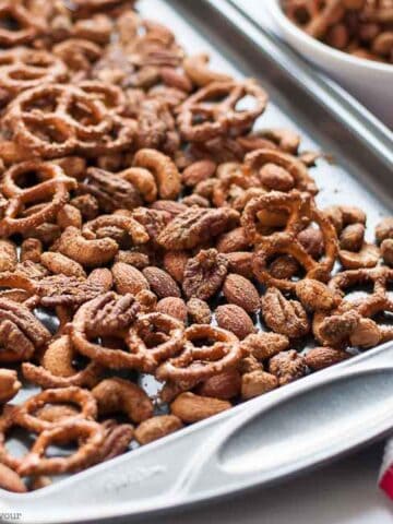 A spicy snack mix made with pretzels and mixed nuts on a baking sheet.