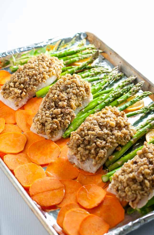 Maple Walnut Crusted Sheet Pan Halibut with sweet potato rounds and asparagus spears on a sheet pan