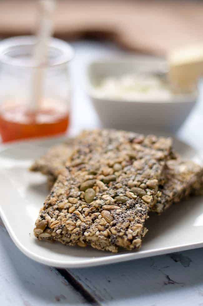 Multi-seed snack crackers on a plate with goat cheese.