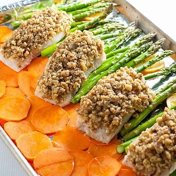 Maple walnut-crusted halibut on a sheet pan with thinly sliced sweet potatoes and asparagus spears.