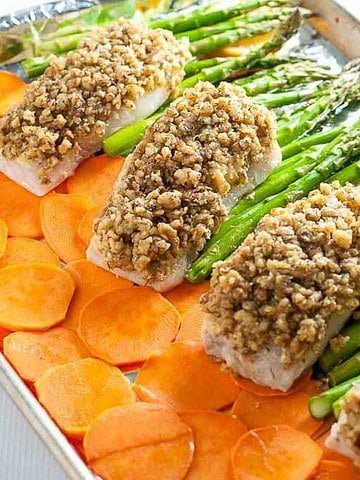 Maple walnut-crusted halibut on a sheet pan with thinly sliced sweet potatoes and asparagus spears.