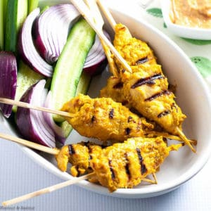 Chicken Satay skewers with red onion and cucumber slices in a white bowl
