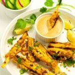 Dipping a chicken satay skewer into a bowl of peanut dipping sauce.