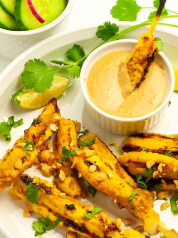 Dipping a chicken satay skewer into a bowl of peanut dipping sauce.
