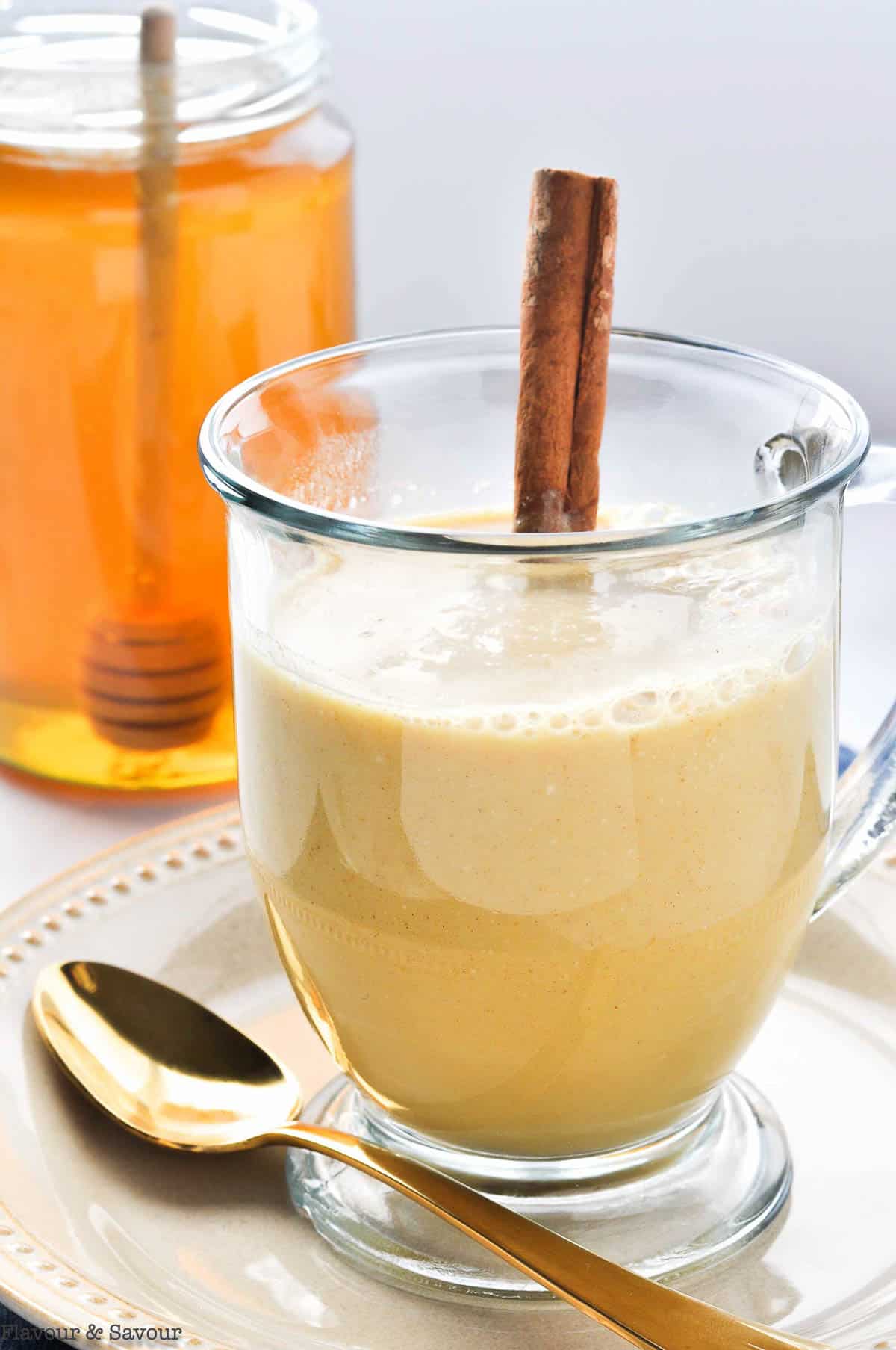 a glass mug of warm turmeric cinnamon milk with a cinnamon stick