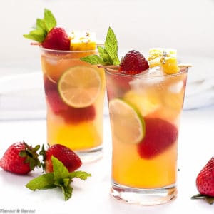 Two glasses of Grilled Pineapple Strawberry Sangria with lime slices, strawberries, pineapple and mint leaves