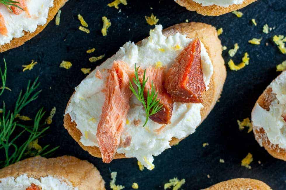 Close up view of Smoked Salmon Crostini with Whipped Honey Lemon Goat Cheese garnished with lemon zest and fresh dill.