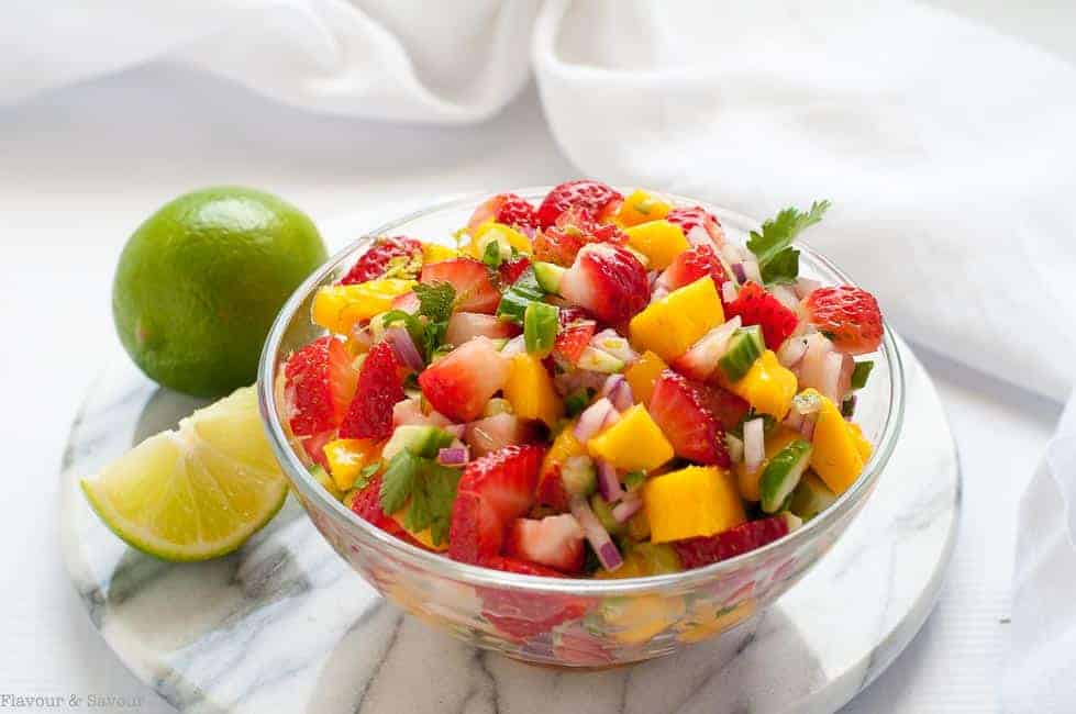 A bowl of Strawberry Mango Salsa with a quartered lime nearby