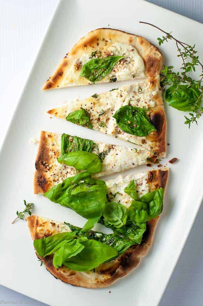 Whipped Goat Cheese Sesame Flatbread with Za'atar garnished with fresh basil and thyme and sliced into triangles.