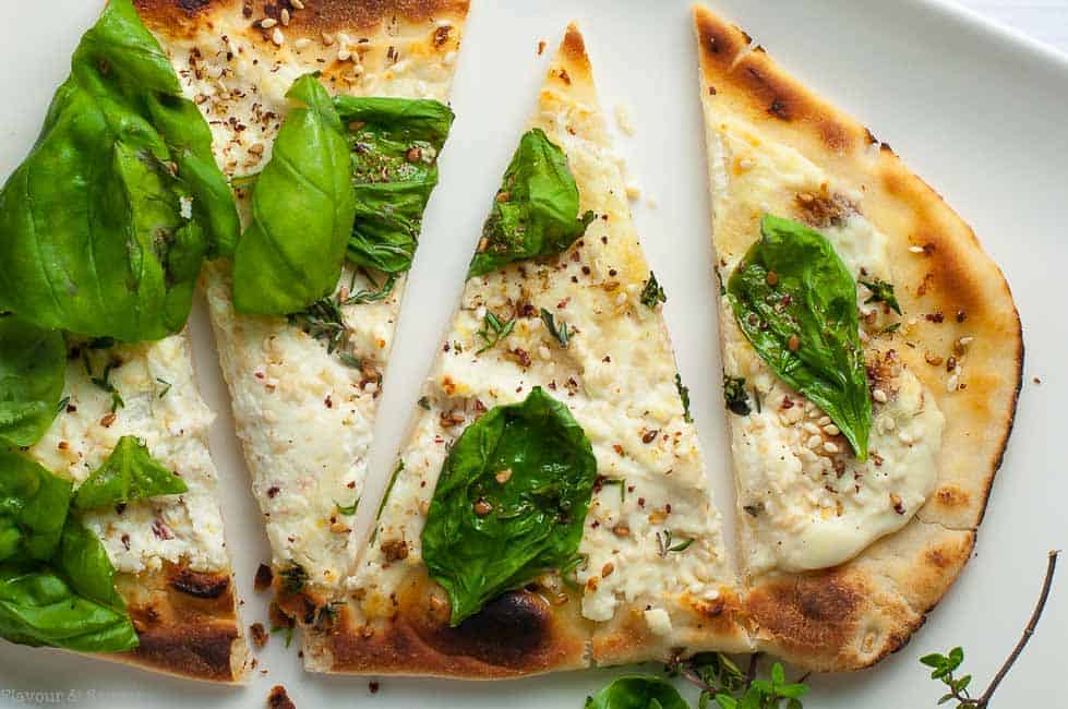 Whipped Goat Cheese Sesame Flatbread with Za'atar with fresh basil cut into wedges.