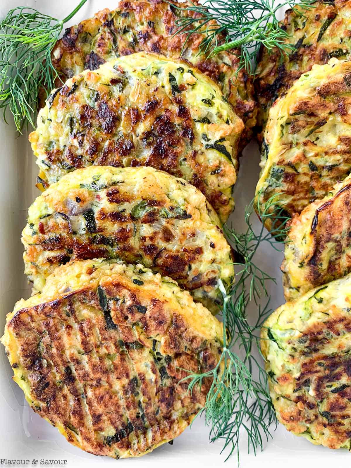 Close up view of 8 zucchini patties on a white platter