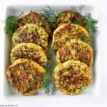 8 zucchini patties on a plate with herbs