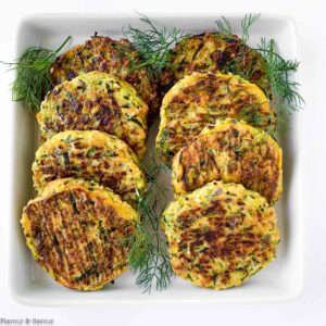 8 zucchini patties on a plate with herbs