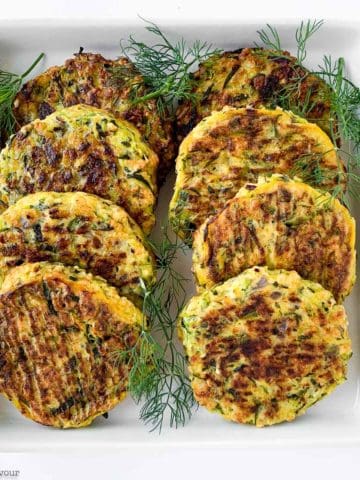 8 zucchini patties on a plate with herbs