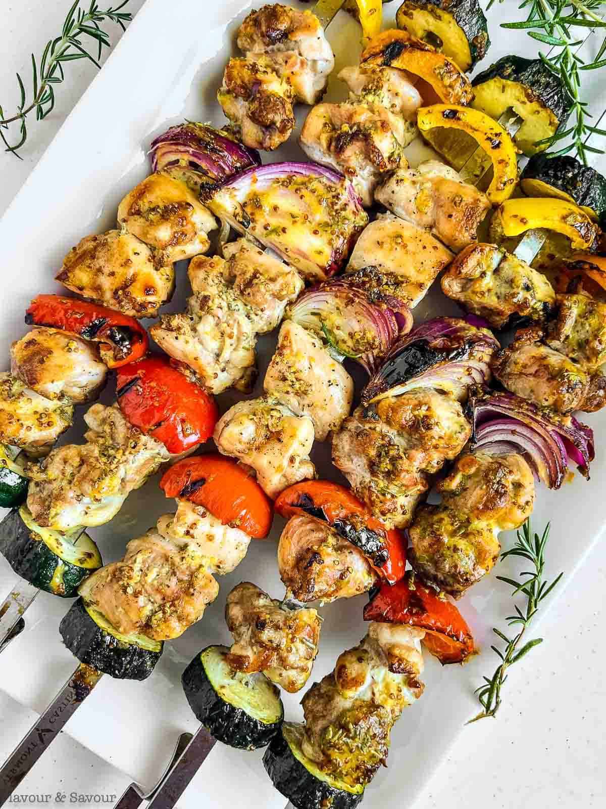 Grilled rosemary mustard chicken kabobs on a white platter.