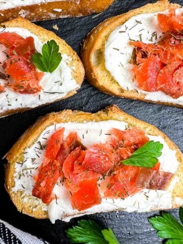 Three smoked salmon crostini appetizers on a black slate board.