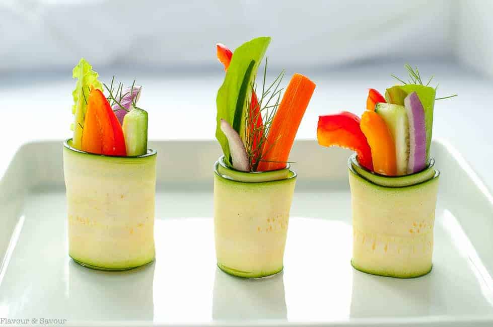 Fresh Zucchini Roll-ups with raw colourful vegetables on a white tray