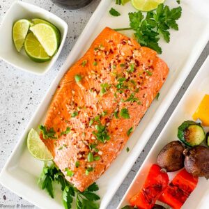 Honey Chili Lime Glazed Salmon on a platter with limes and vegetable kabobs.