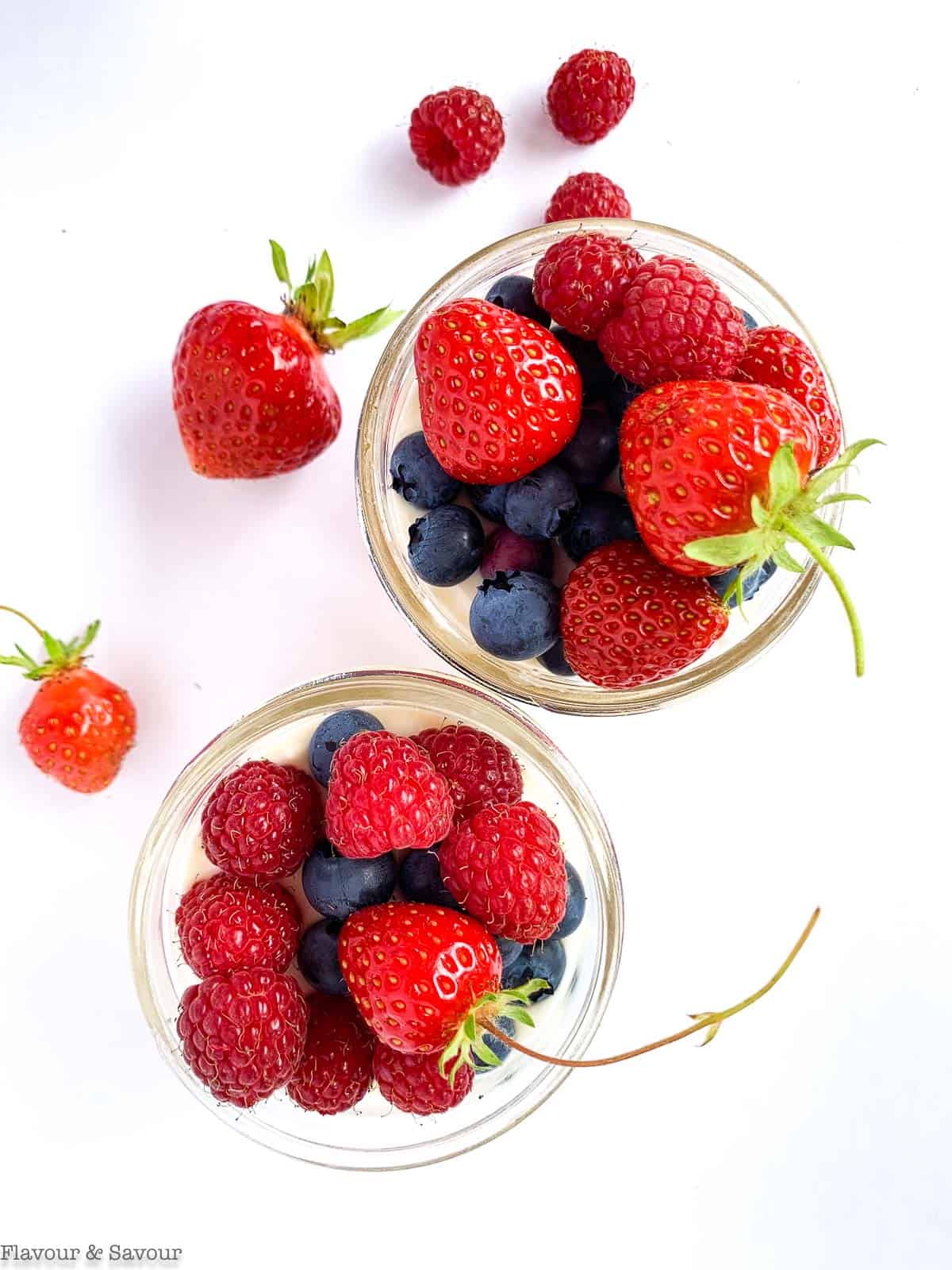 Overhead view of 2 small Mason jars filled with no-bake cheesecake and topped with fresh blueberries, strawberries and raspberries