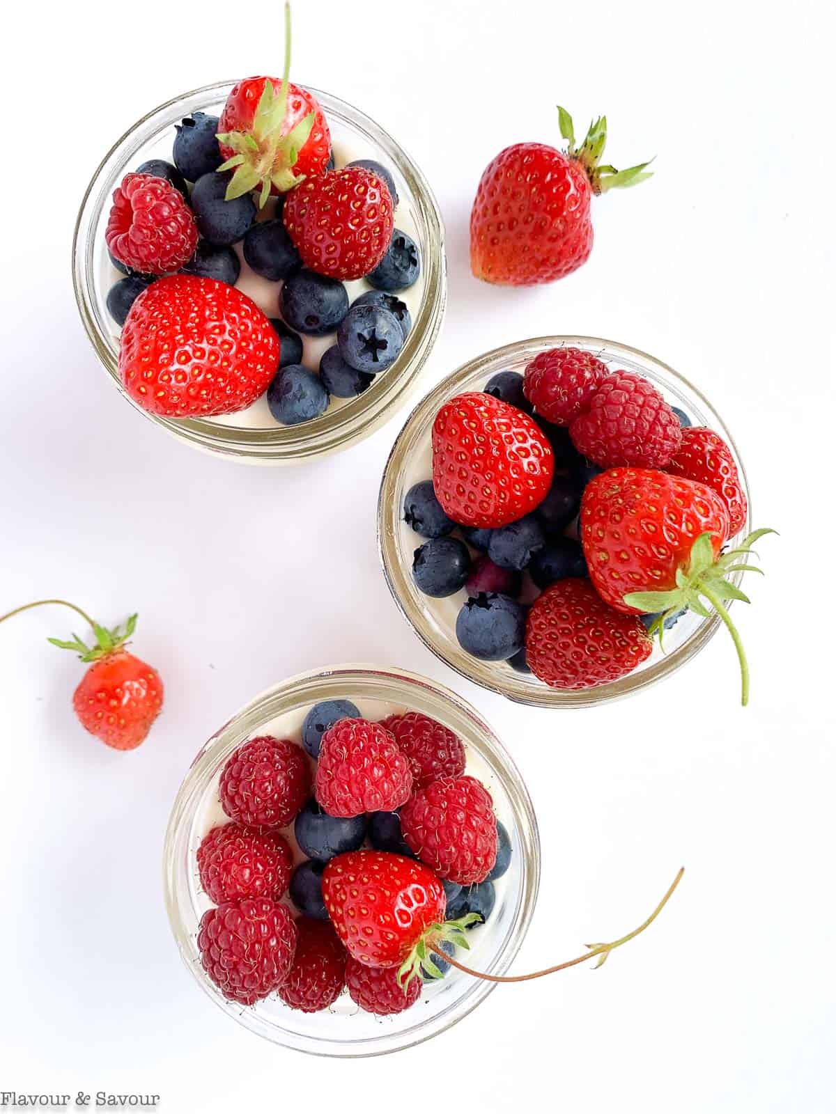 3 small Mason jars filled with no-bake cheesecake and topped with fresh blueberries, strawberries and raspberries