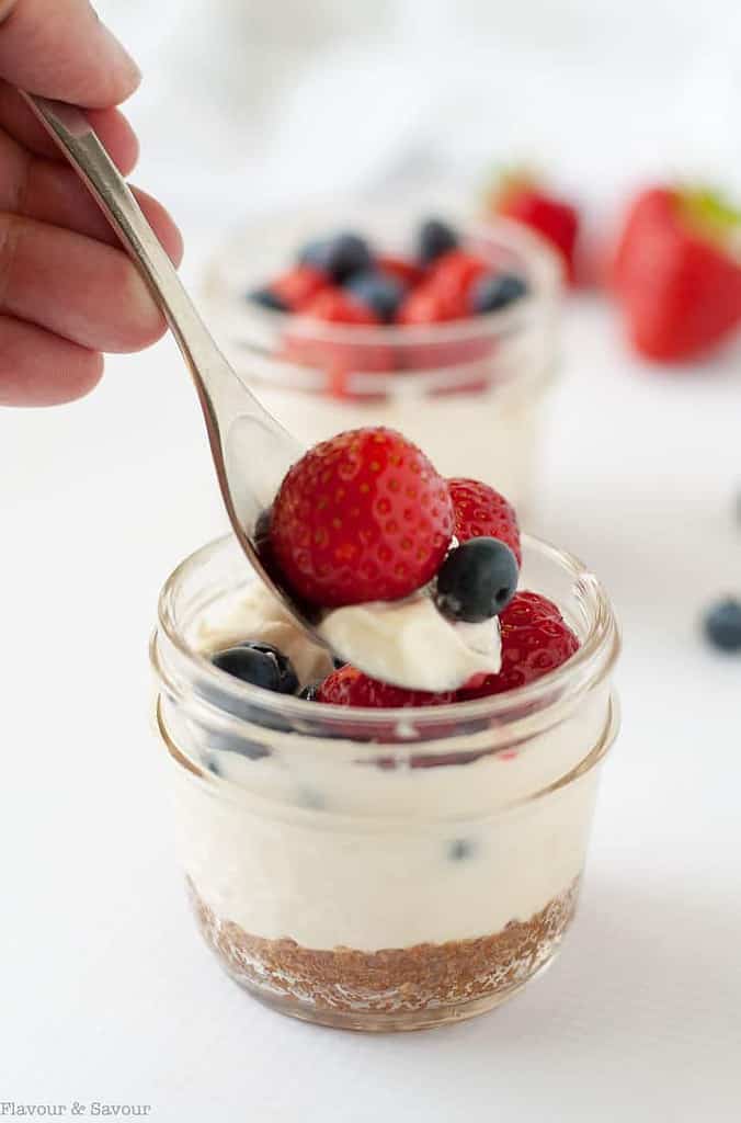 a spoonful of no-bake cheesecake with strawberries and blueberries in a small Mason jar