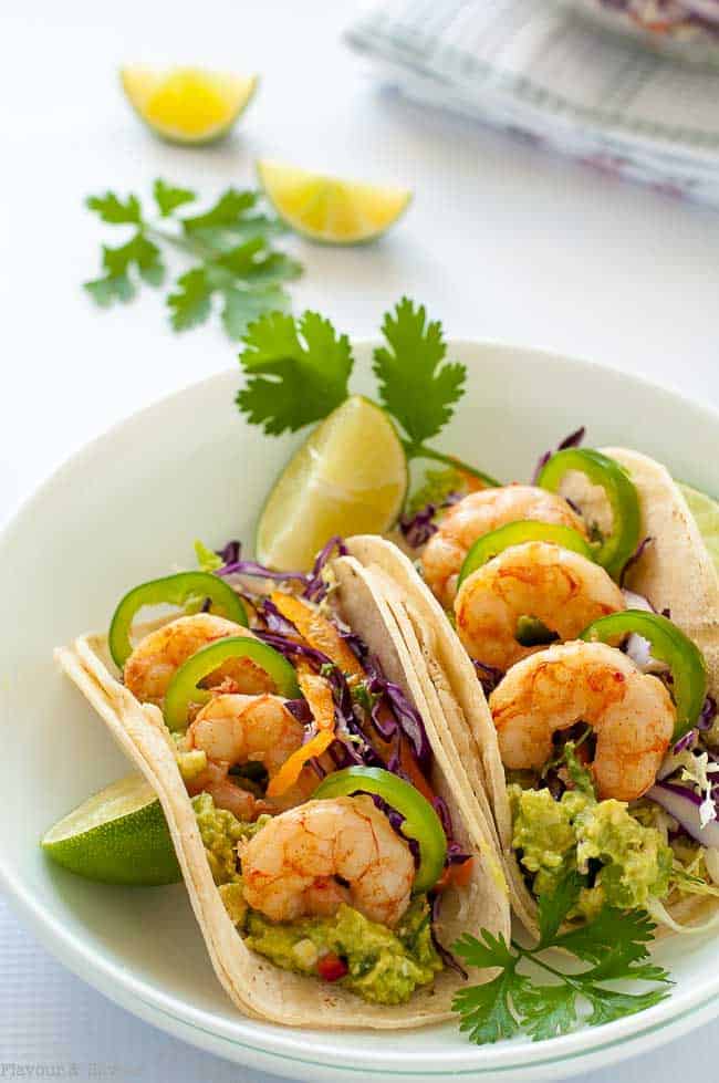 Shrimp Tacos with Cilantro Lime Slaw in a white bowl garnished with lime wedges and cilantro leaves