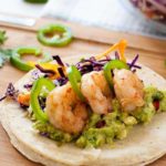 These Shrimp Tacos are loaded with zesty Tomatillo Guacamole and crunchy Cilantro Lime Slaw. They're topped with garlicky buttered shrimp, fresh jalapeño and a squeeze of lime.